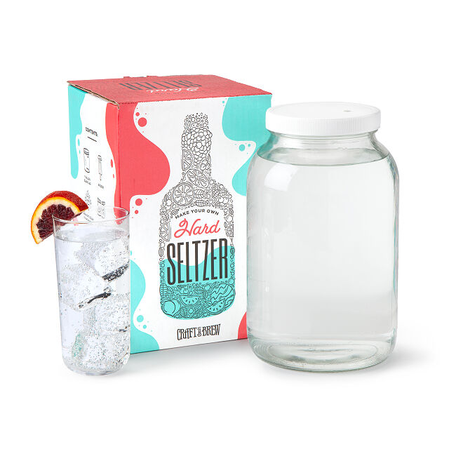 Hard seltzer kit sitting with a large glass jug, and a glass of hard seltzer with a grapefruit slice