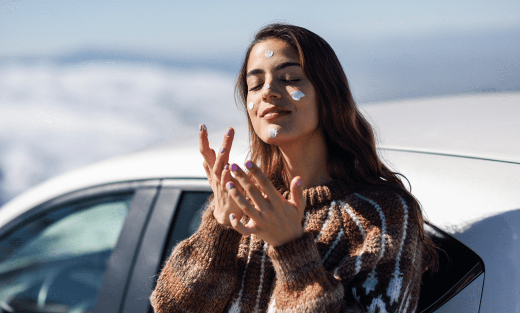 Woman applying sunscreen to her face while wearing a warm looking sweater