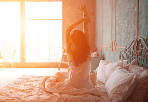 A woman waking up in bed, stretching in the sunlight