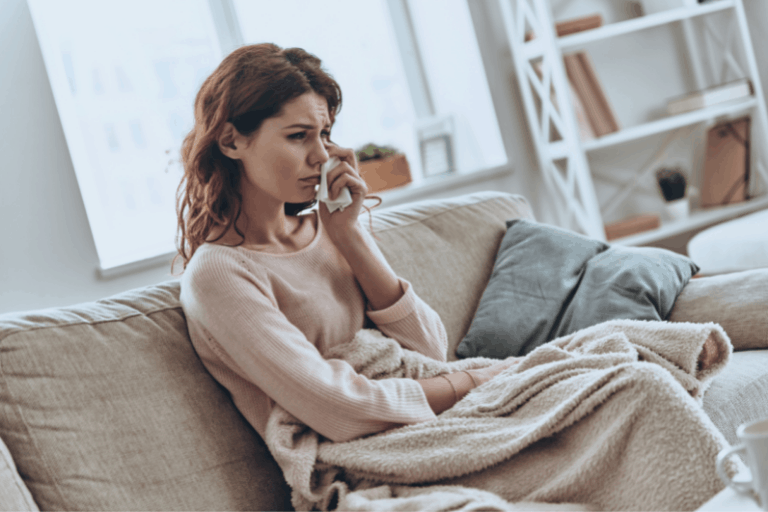 Woman sitting on a sofa with a blanket on her lap, looking sad