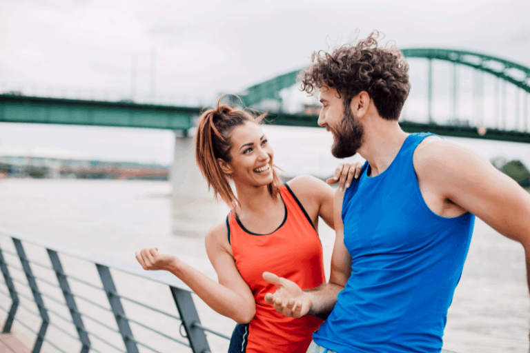 Man and woman in workout attire, chatting on a bridge