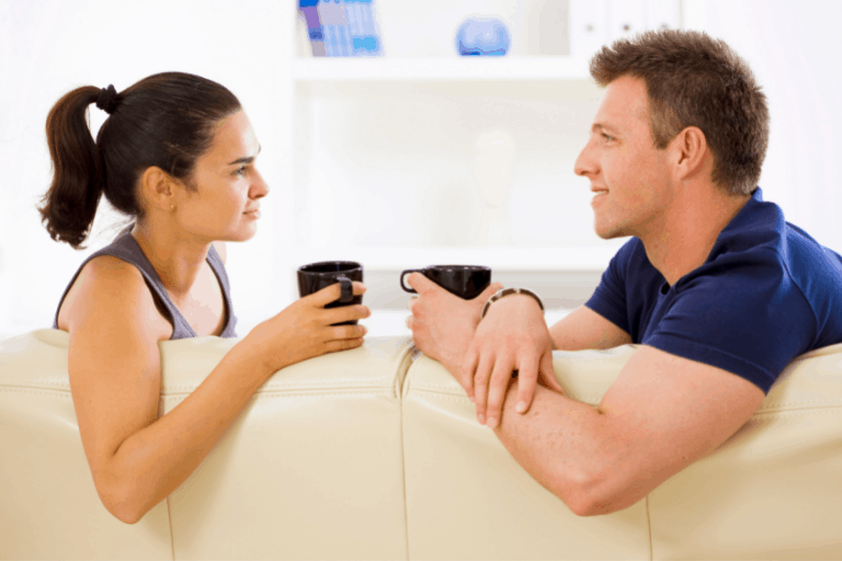 Man and woman having coffee together on a sofa, looking at each other
