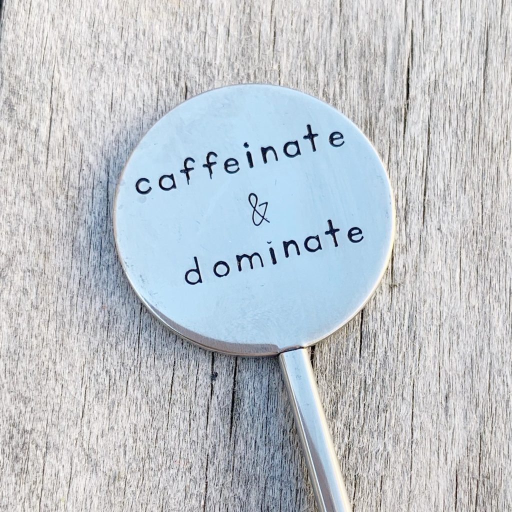 Silver coffee stirrer reading, "caffeinate & dominate"