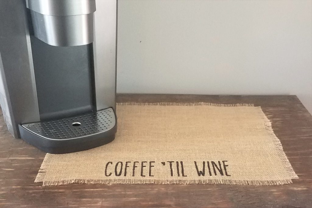 Burlap coffee mat that reads "Coffee 'til Wine," with a Keurig coffee maker sitting on it