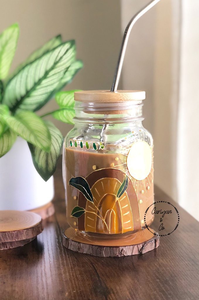 Clear glass jar with a rainbow painted on it, full of iced coffee, with a lid and straw