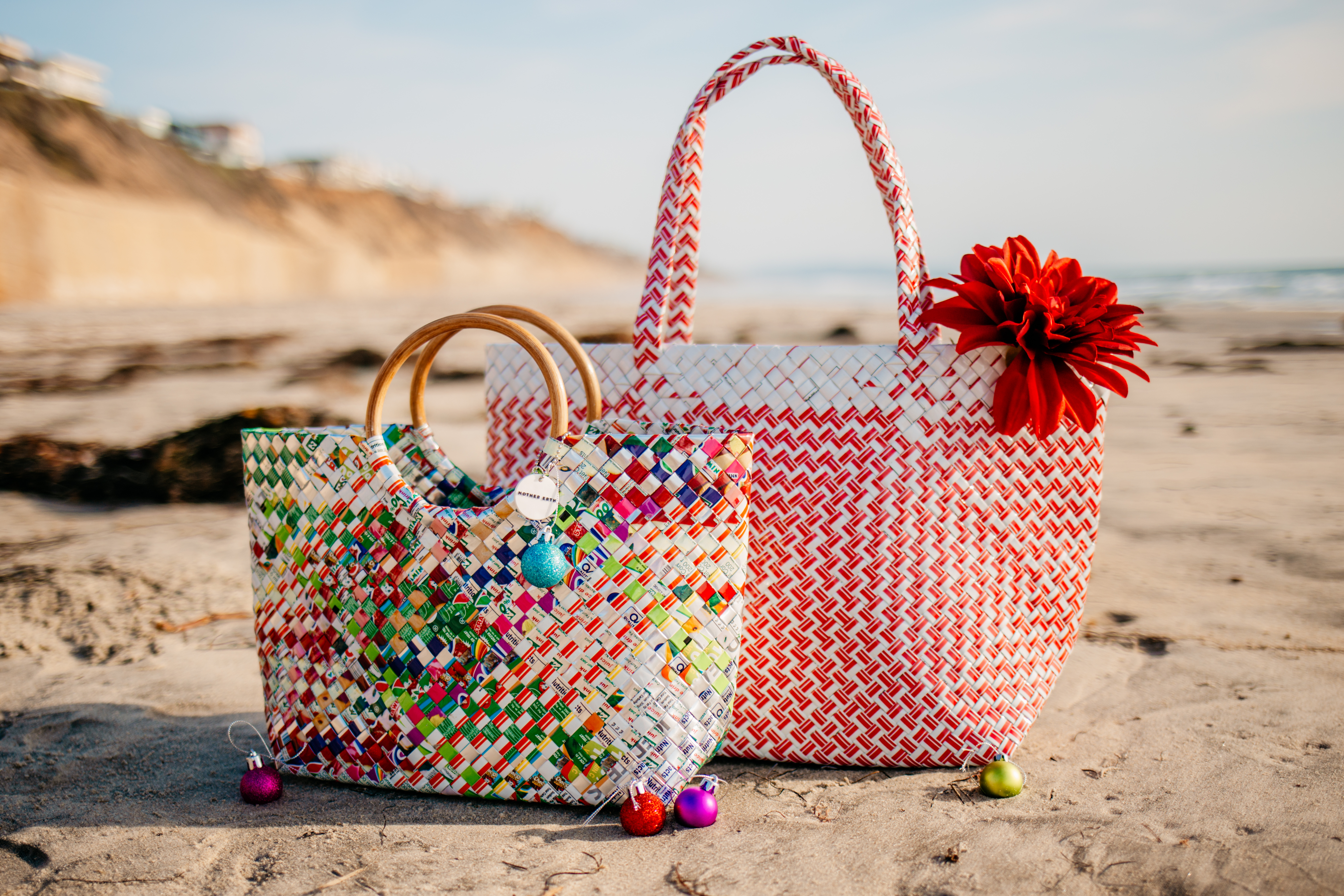 Two sustainable purses made of upcycled plastic on the beach, with small Christmas ornaments