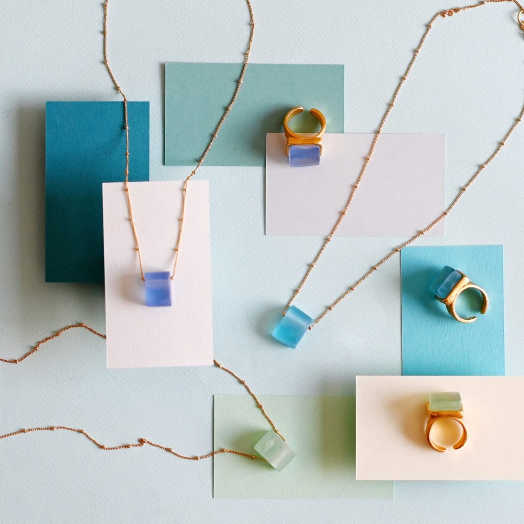 Sea glass necklaces on gold chains, laid out on brightly colored square pieces of paper