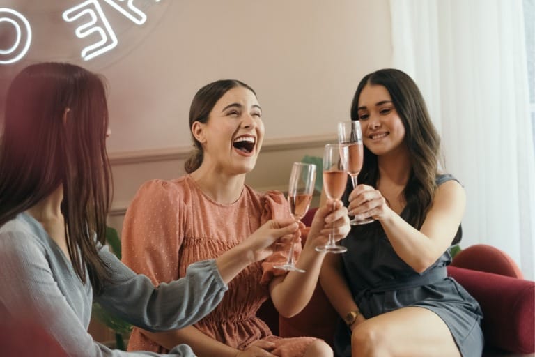 Three women sitting together and cheering with champagne for Galentine's Day as a singles Valentine's Day idea