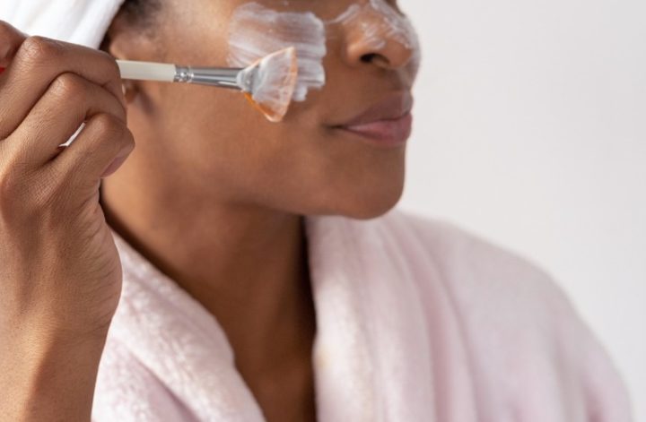 Woman in bathrobe applying a face mask with a makeup brush
