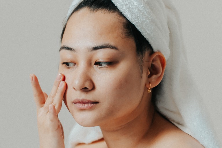 Woman with her hair in a towel applying skincare to her face
